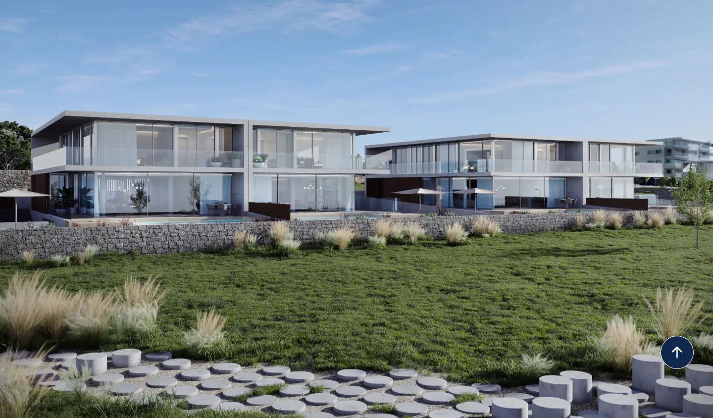 Two-story modern homes with large windows, stone walls, and green lawn under a blue sky.