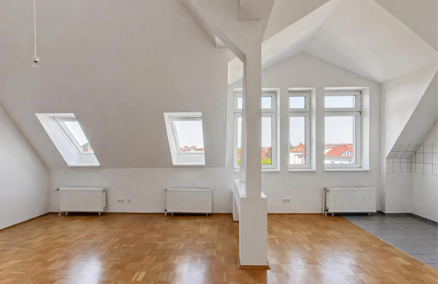 Bright, empty attic apartment with white walls, wood floors, and skylights. A white support beam divides the space.
