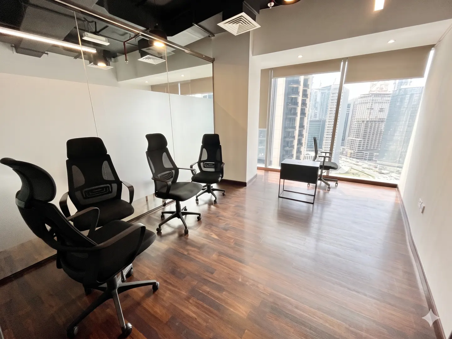 Office space with black chairs on a wood floor, a desk, and a large window with a city view.