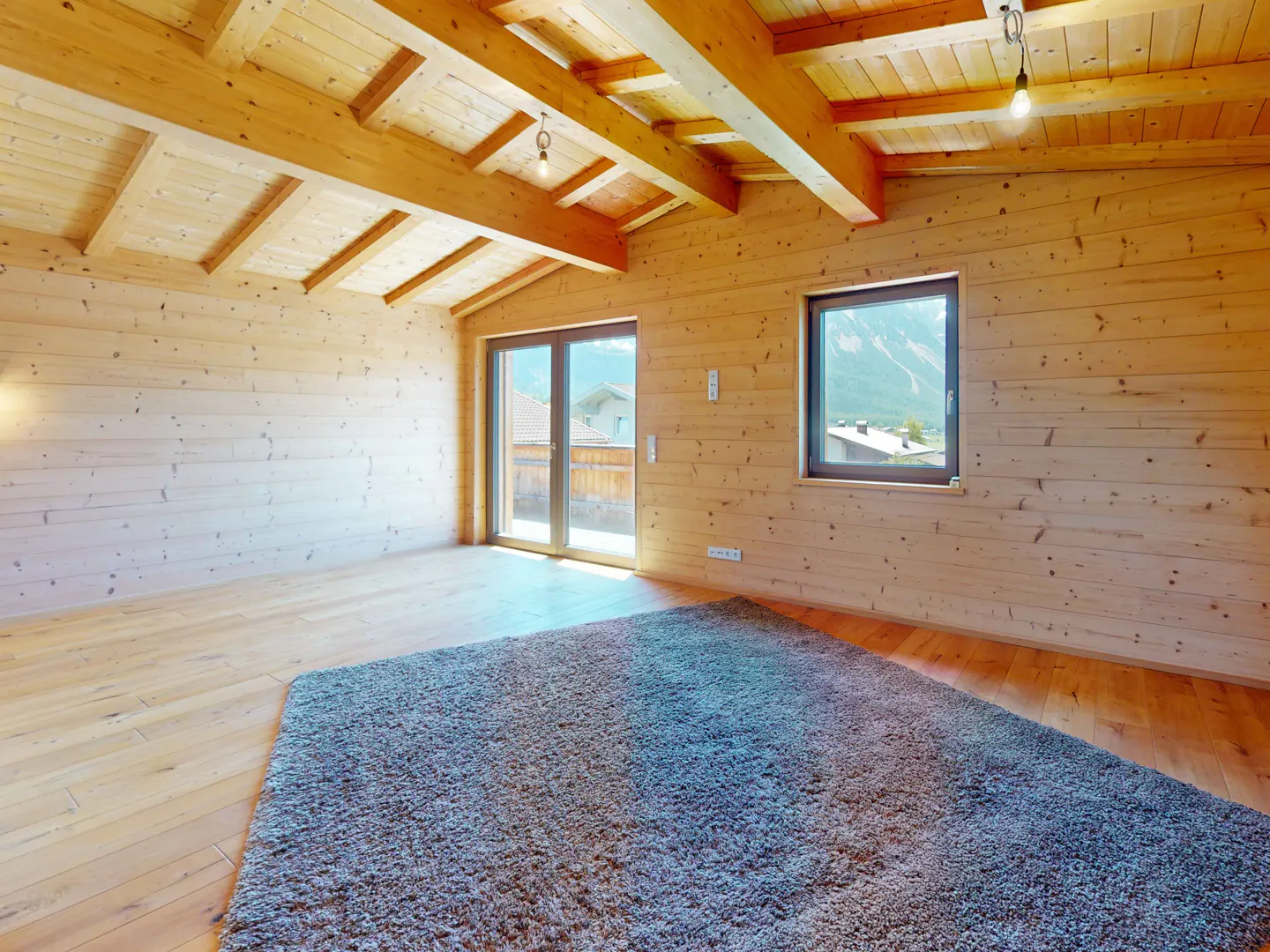 A room with wood walls, ceiling, and floor, a gray rug, a window, and a sliding glass door.