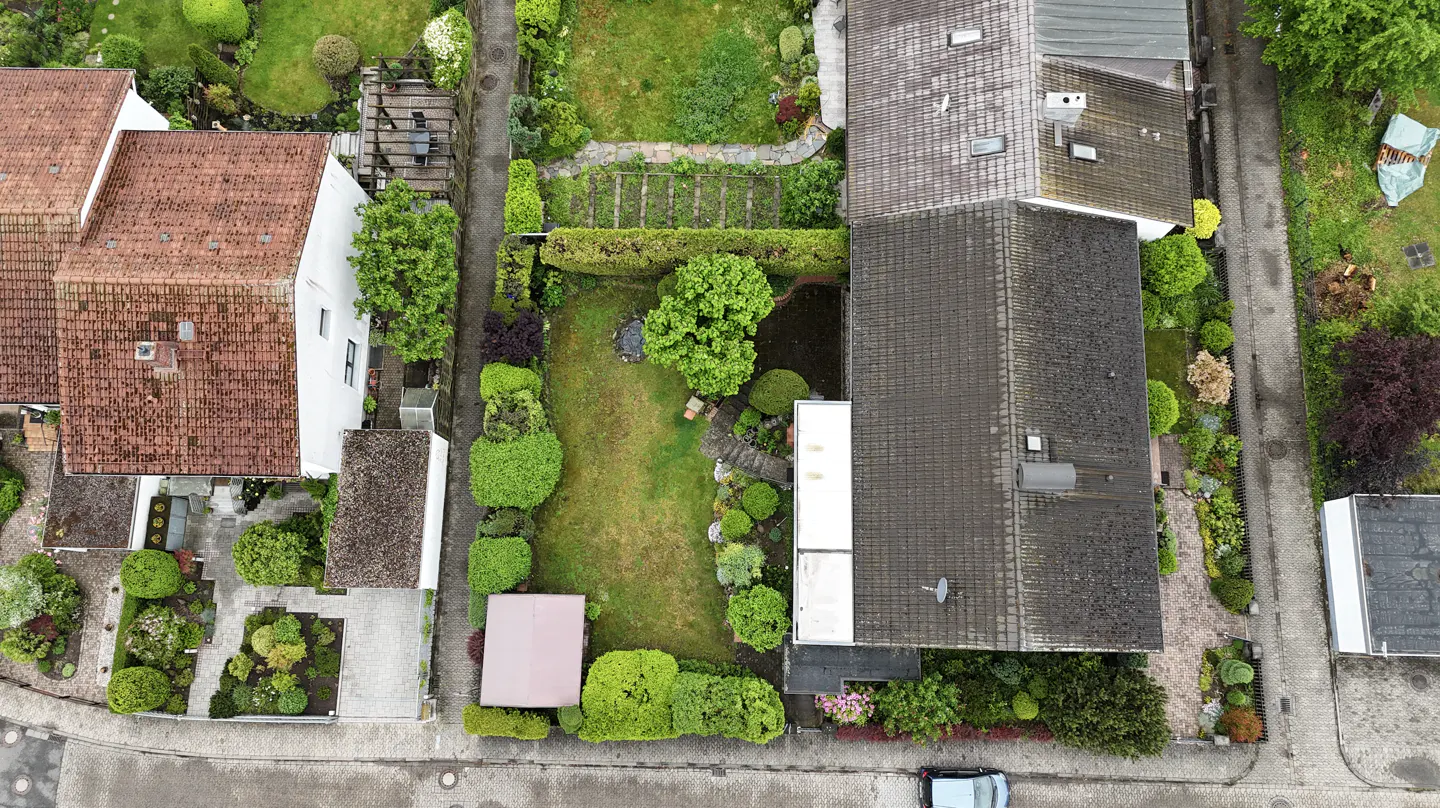Aerial view of two residential houses with tiled roofs separated by a narrow garden path and lush green landscaping.