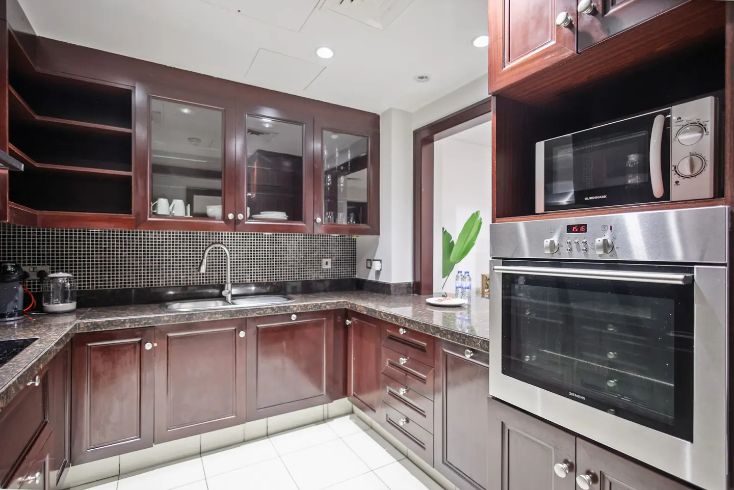 A modern kitchen with dark wood cabinets, stainless steel appliances, and white tile flooring.