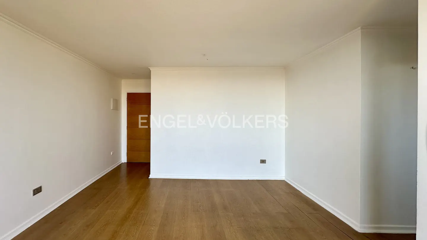 Empty room with wood floors, white walls, and a wood door. Engel & Völkers logo is superimposed on the wall.