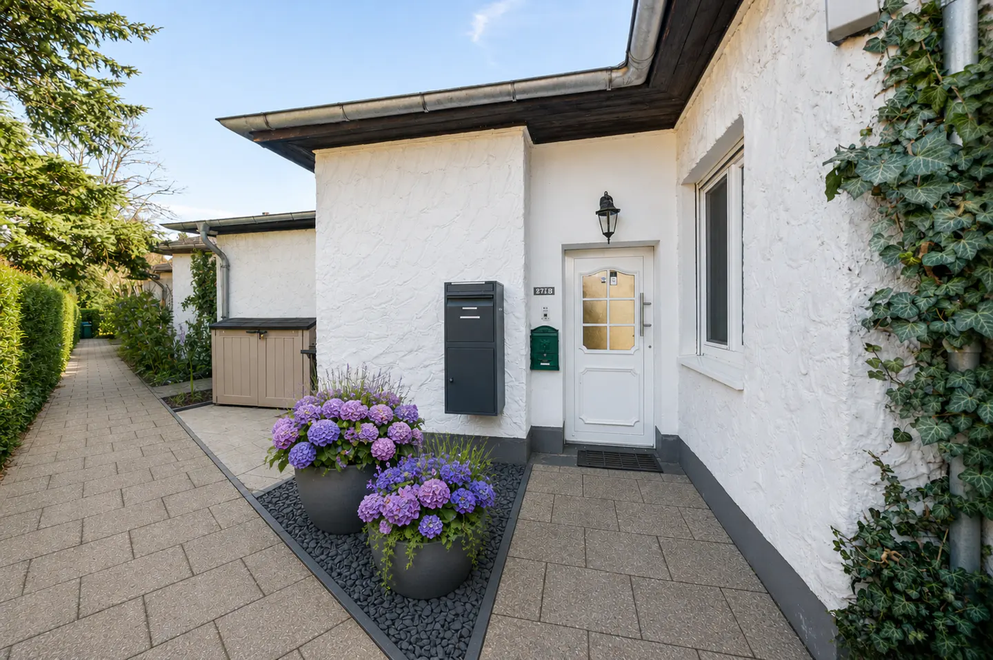 Exterior of a white house with a white door, black mailbox, and purple hydrangeas in gray pots.