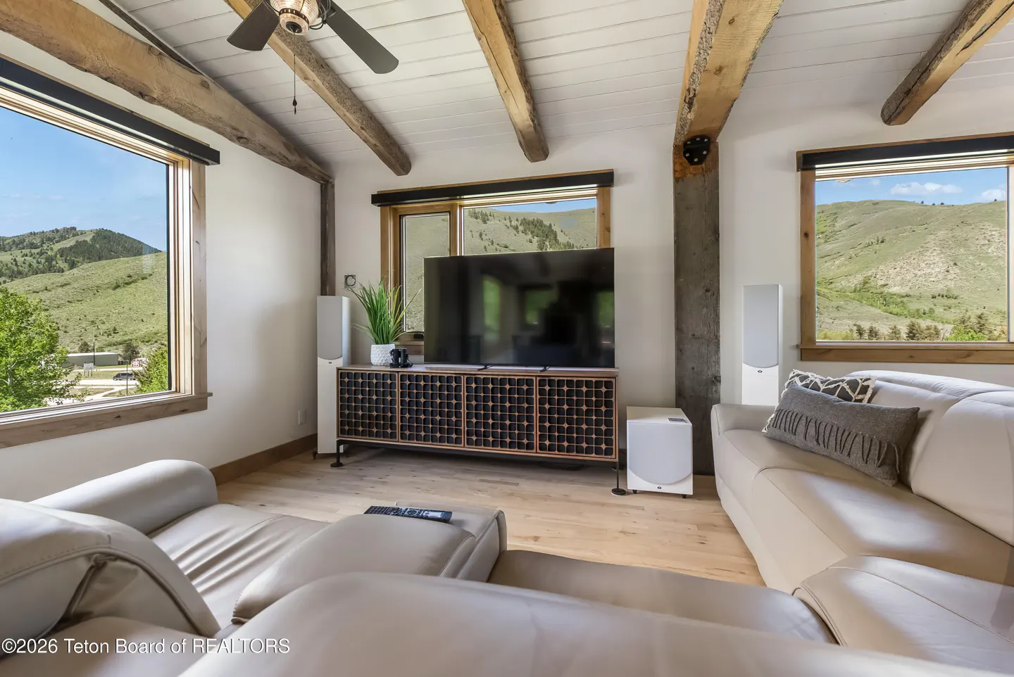 Living room with light leather sofas, large TV on a patterned console, and expansive windows showing mountain views.