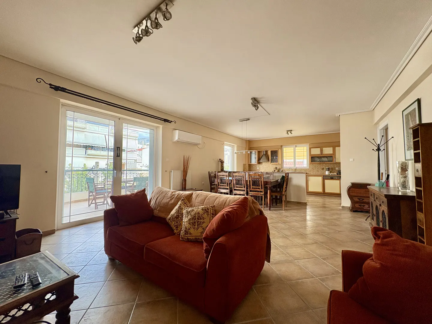 Open-concept living space with terracotta sofa, dining table, and kitchen. Sliding glass doors lead to a balcony.