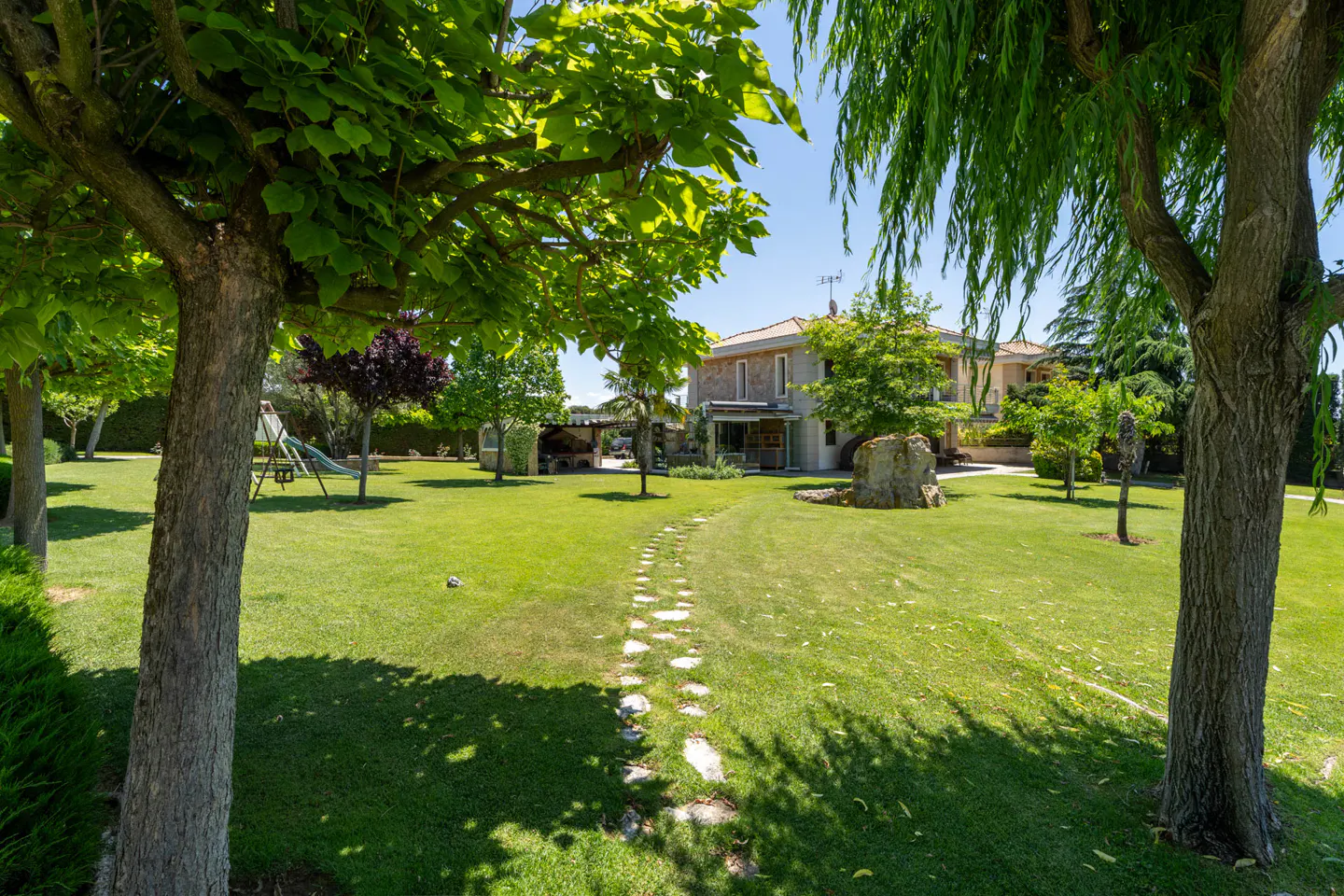 Stone path leads to a two-story house with a green lawn and trees on a sunny day.