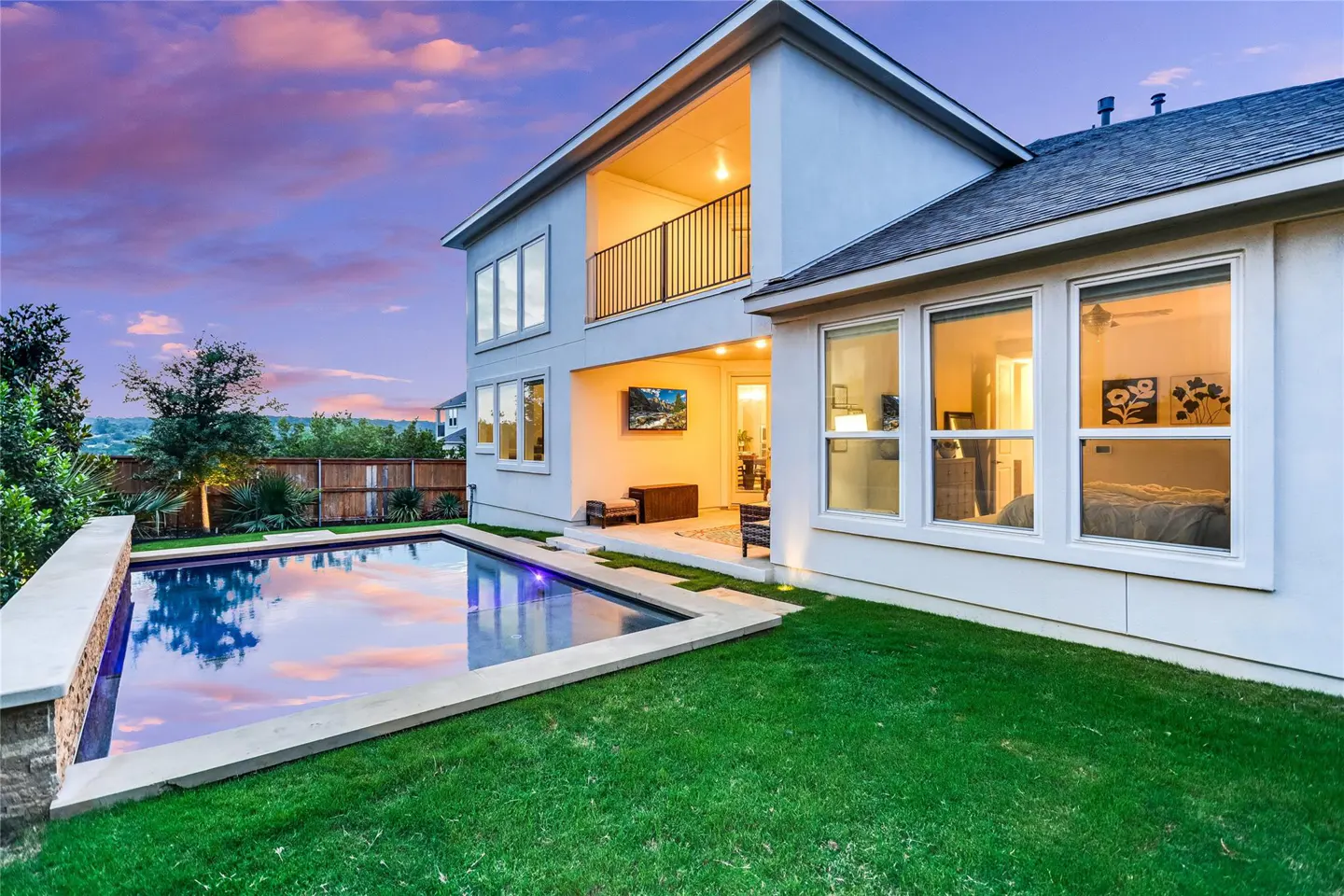 Backyard view of a two-story white house with a pool, green lawn, and patio at dusk.