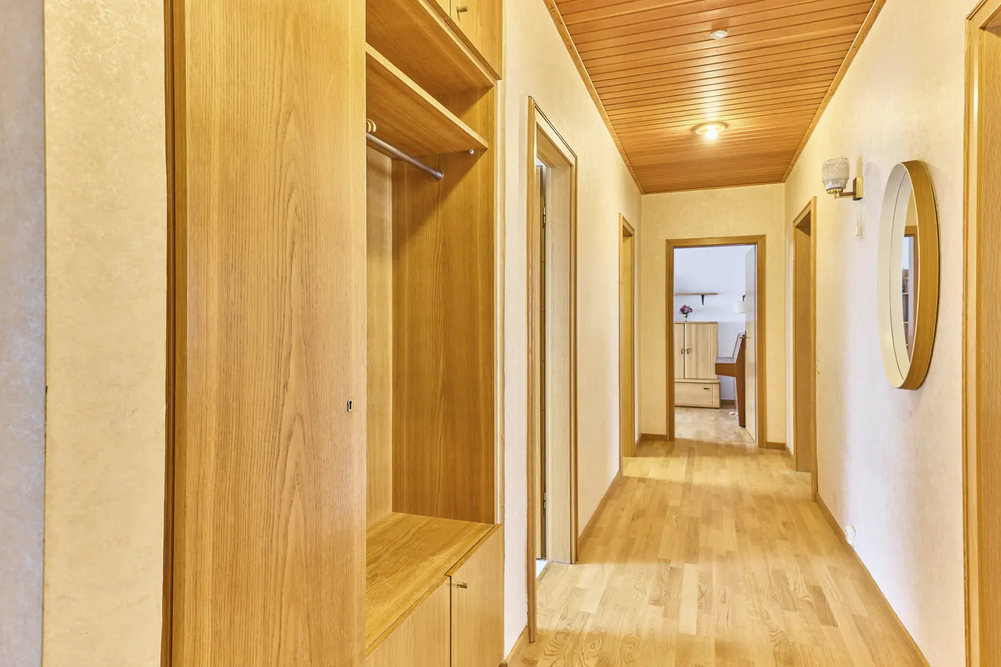 Hallway with light wood floors, wood paneled ceiling, and a built-in wood closet with shelves and hanging space.