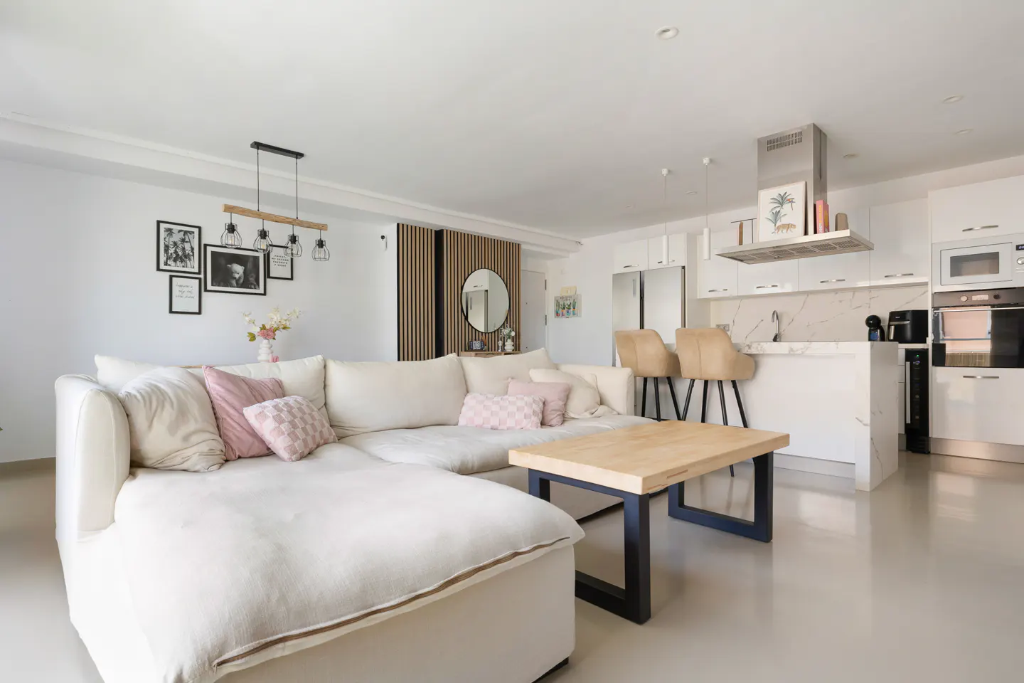 Open-concept living space with a white sectional sofa, wood coffee table, and kitchen island with bar stools.