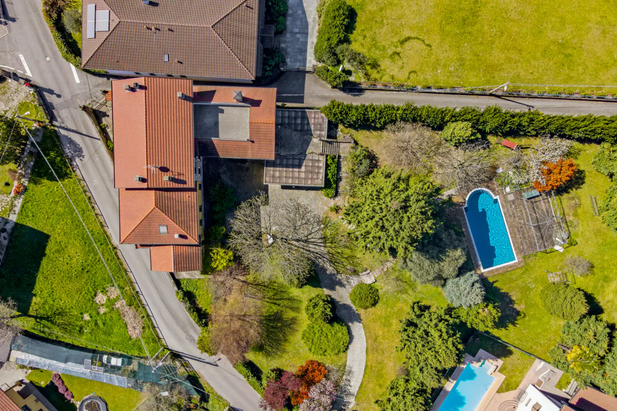 Aerial view of a house with a red tile roof, a blue swimming pool, and green trees and grass.
