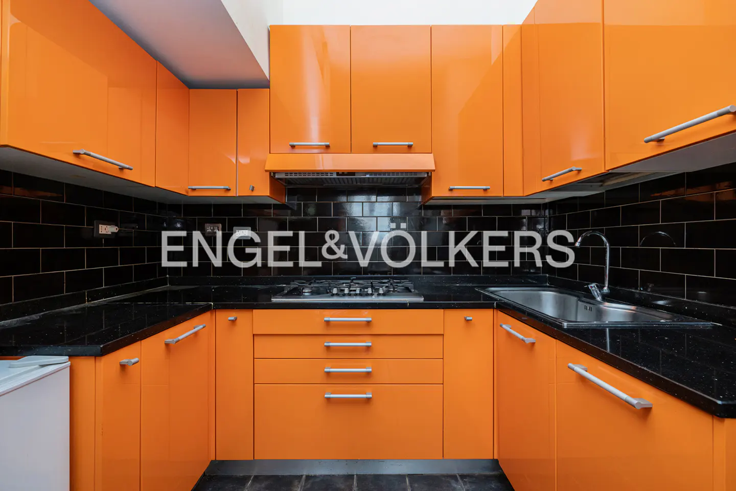 A U-shaped kitchen with orange cabinets, black countertops and backsplash. A stainless steel sink and gas stove are visible.