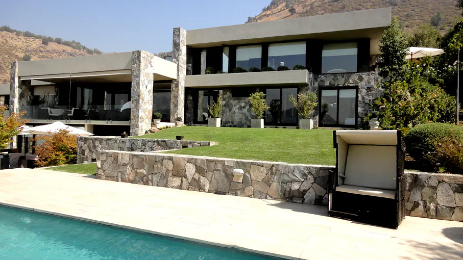 Modern two-story house with stone accents, large windows, and a pool. A beach chair sits near the pool, with a mountain in the background.