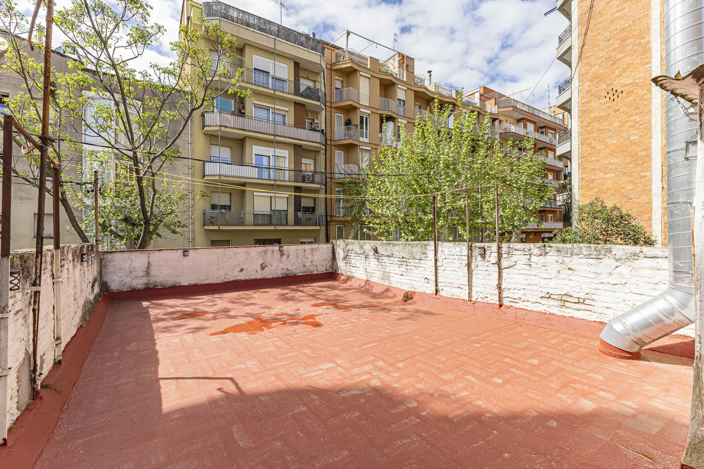 A red brick rooftop with a white brick wall, metal pipes, and apartment buildings in the background.