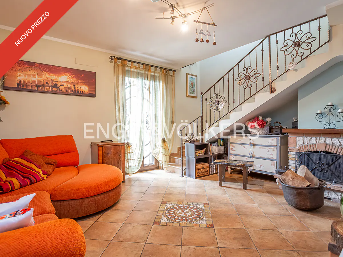 Living room with orange sofa, tiled floor, fireplace, and staircase with ornate metal railing.