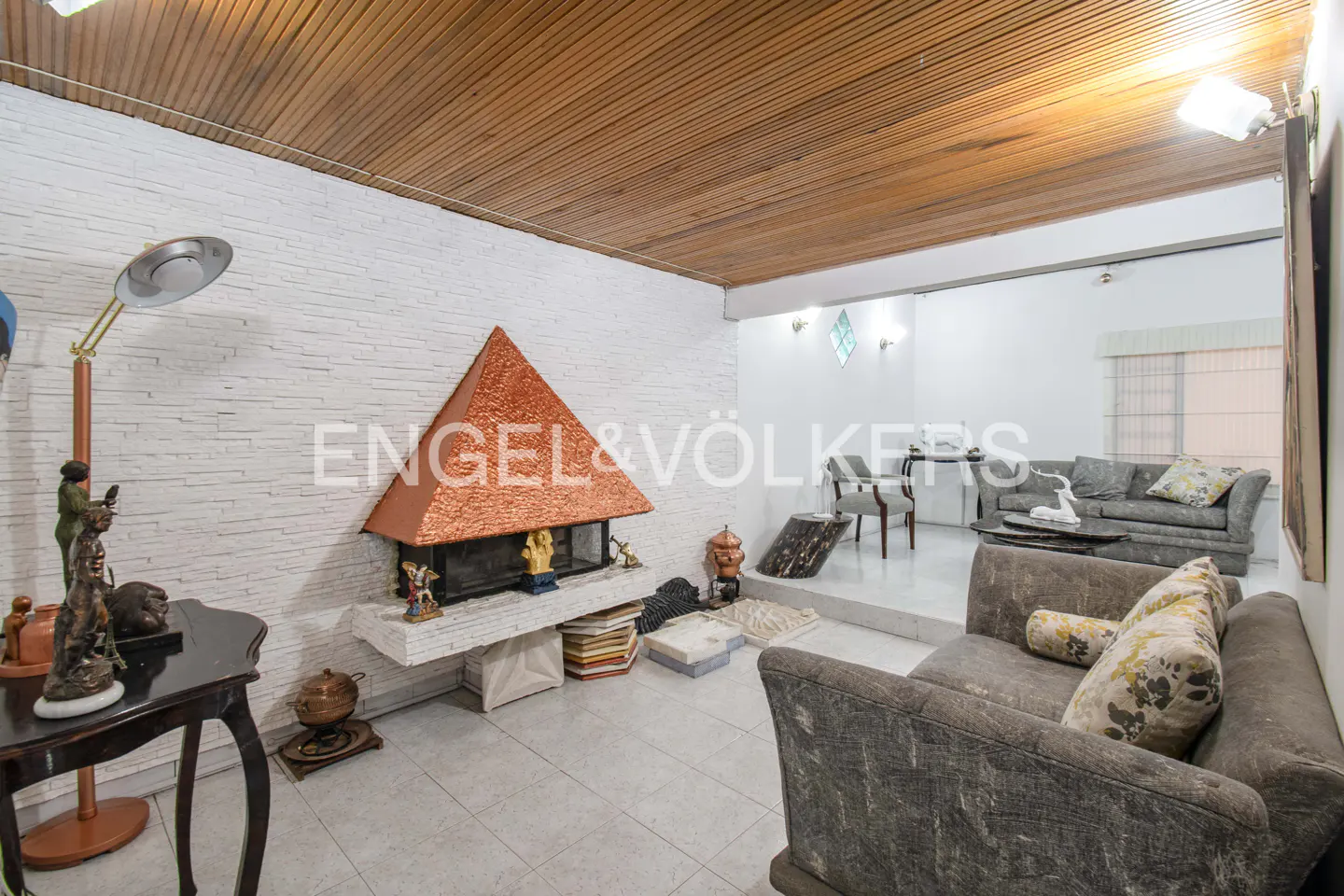A living room with a pyramid-shaped fireplace, gray sofas, and a wooden ceiling.