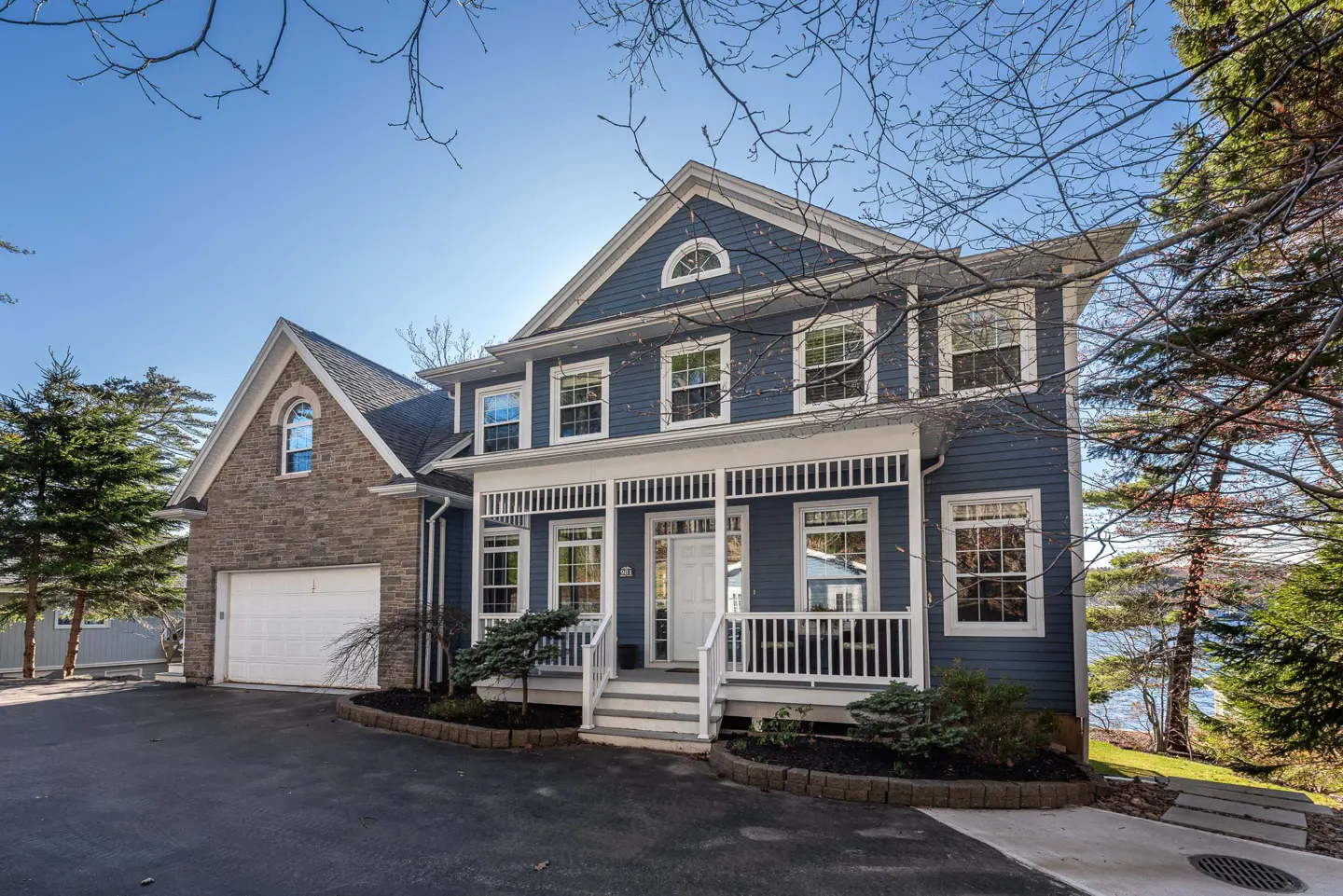 Two-story blue house with white trim, a front porch, and a stone garage under a clear blue sky.
