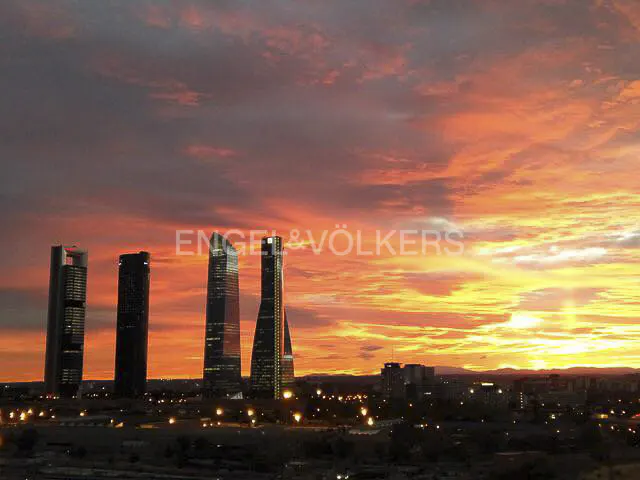 City skyline at sunset with tall buildings silhouetted against a vibrant orange and red sky. Engel & Völkers logo visible.