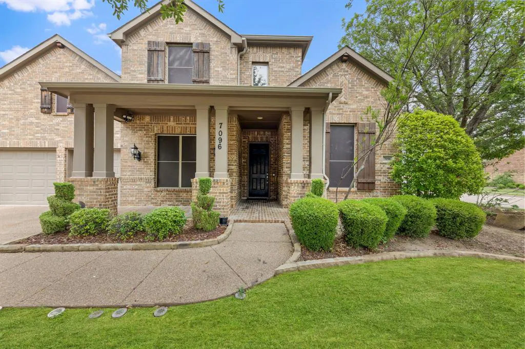 Two-story brick house with a covered porch, dark door, and green lawn.