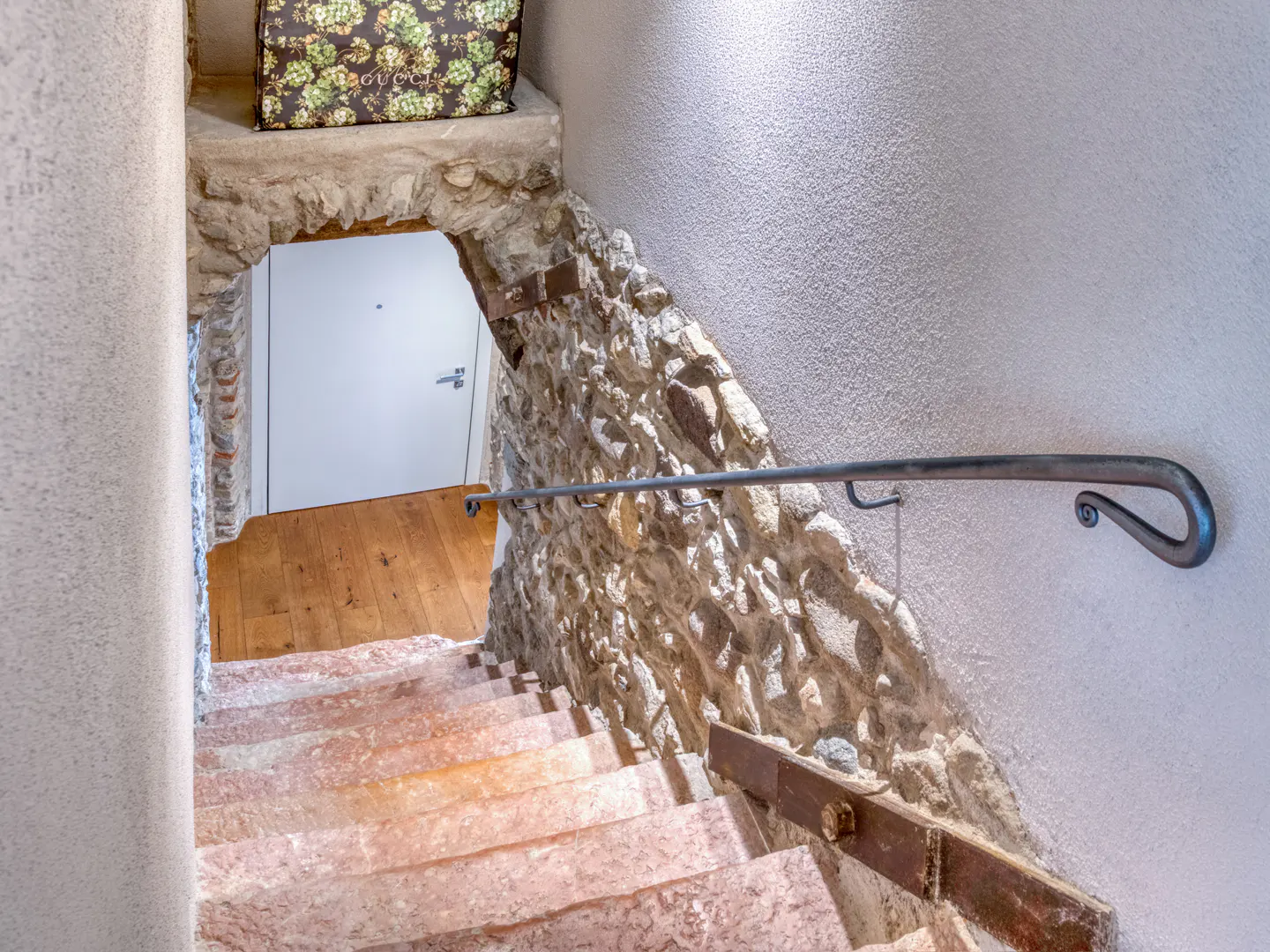 Stone staircase with metal handrail leading to a doorway with wood floors. A Gucci bag sits above the doorway.