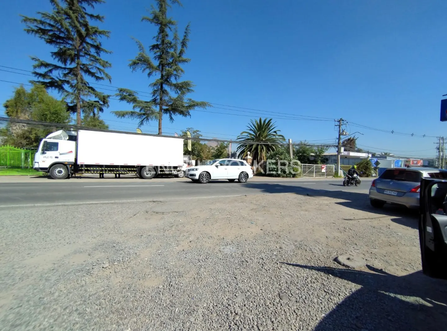 Street view with a white truck and car on the road, under a clear blue sky. "KERS" sign visible in the background.
