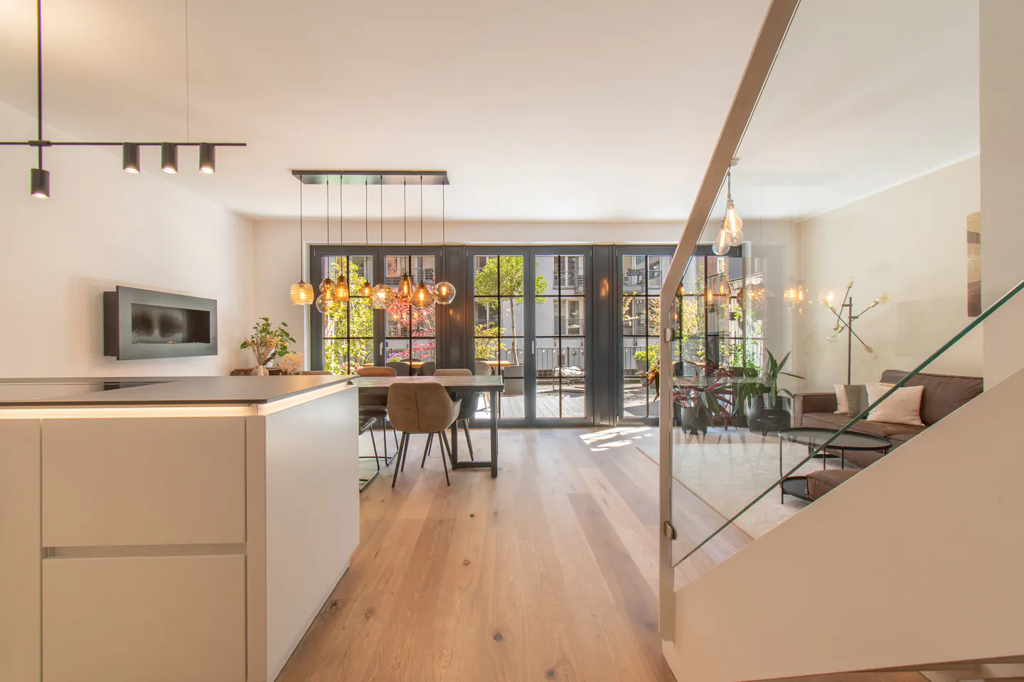 Open-concept living space with a kitchen island, dining table, and living room. Large windows offer a view of the outdoors.