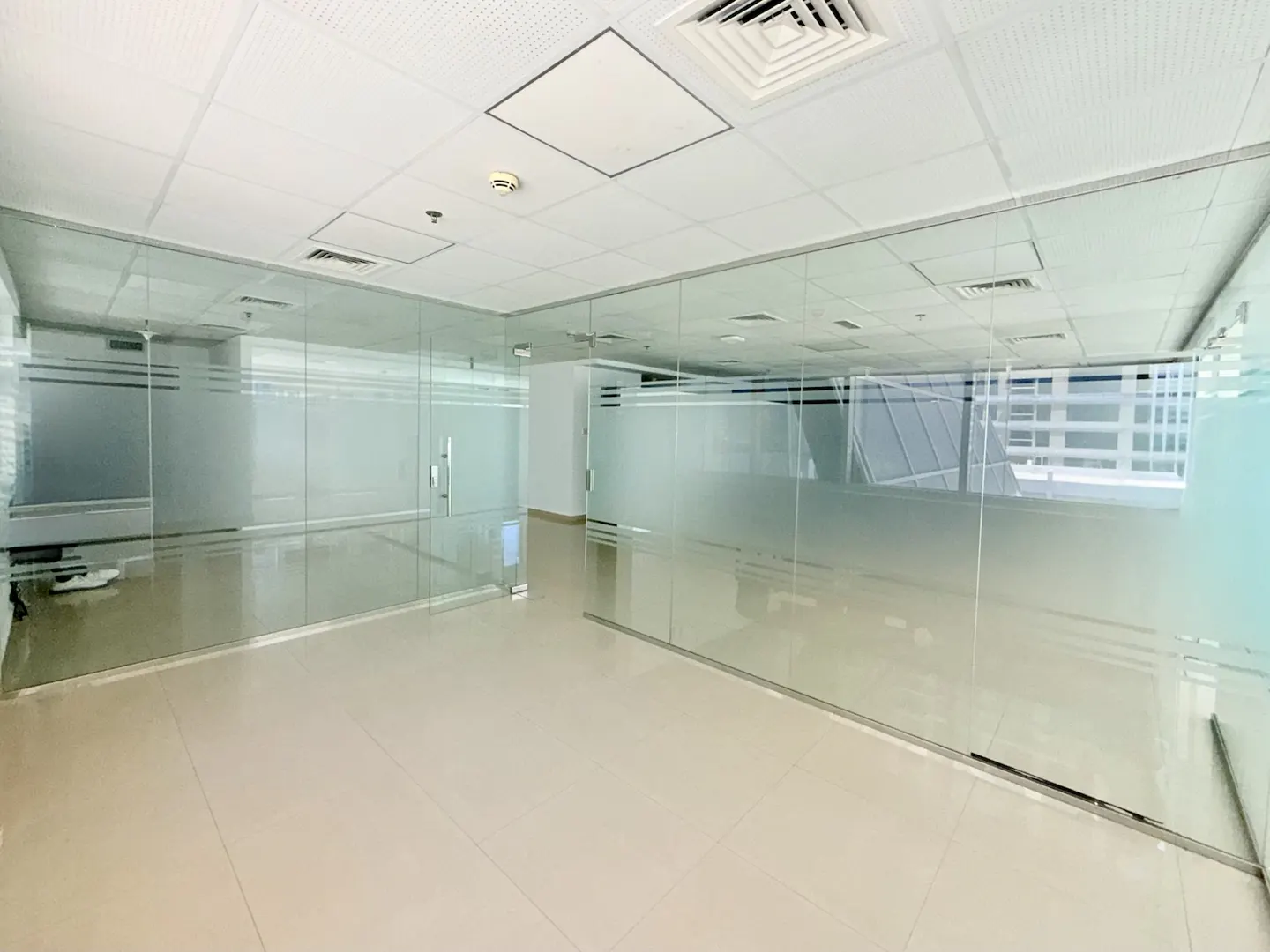 Empty office space with glass walls and doors, beige tile floor, and white ceiling with vents.