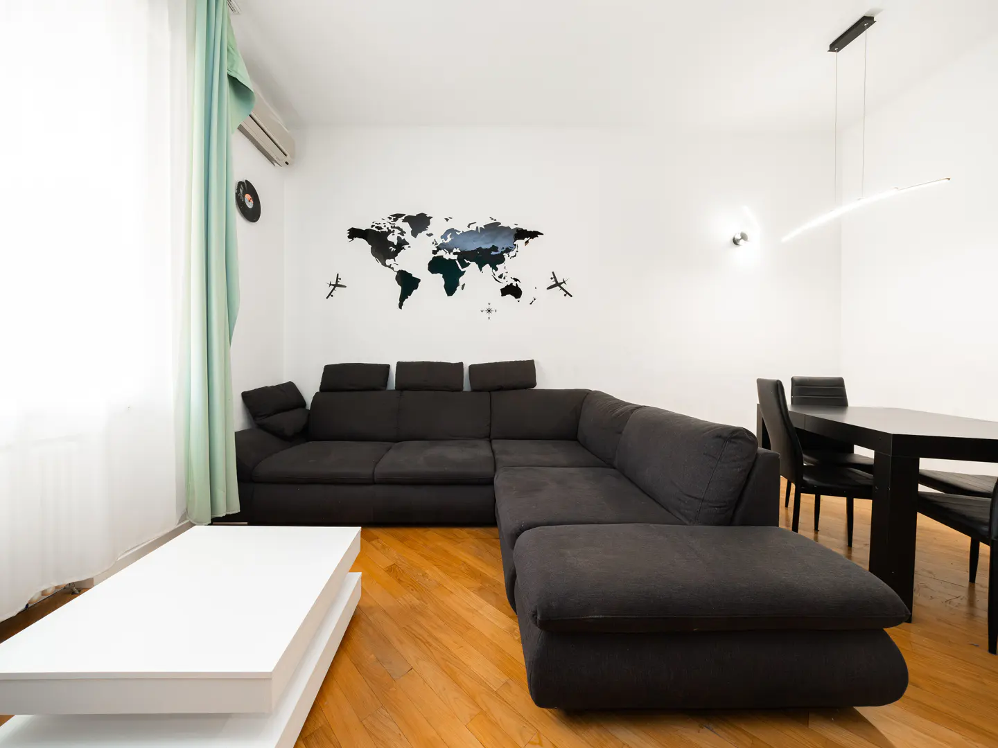 Living room with a dark gray sectional sofa, white coffee table, wood floors, and a world map on the white wall.
