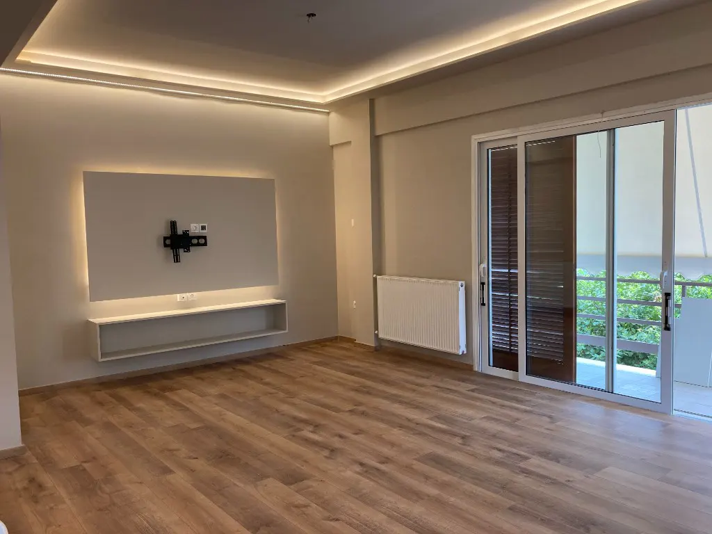 Bright living room with wood floors, sliding glass doors to a balcony, and a wall-mounted TV bracket above a white shelf.