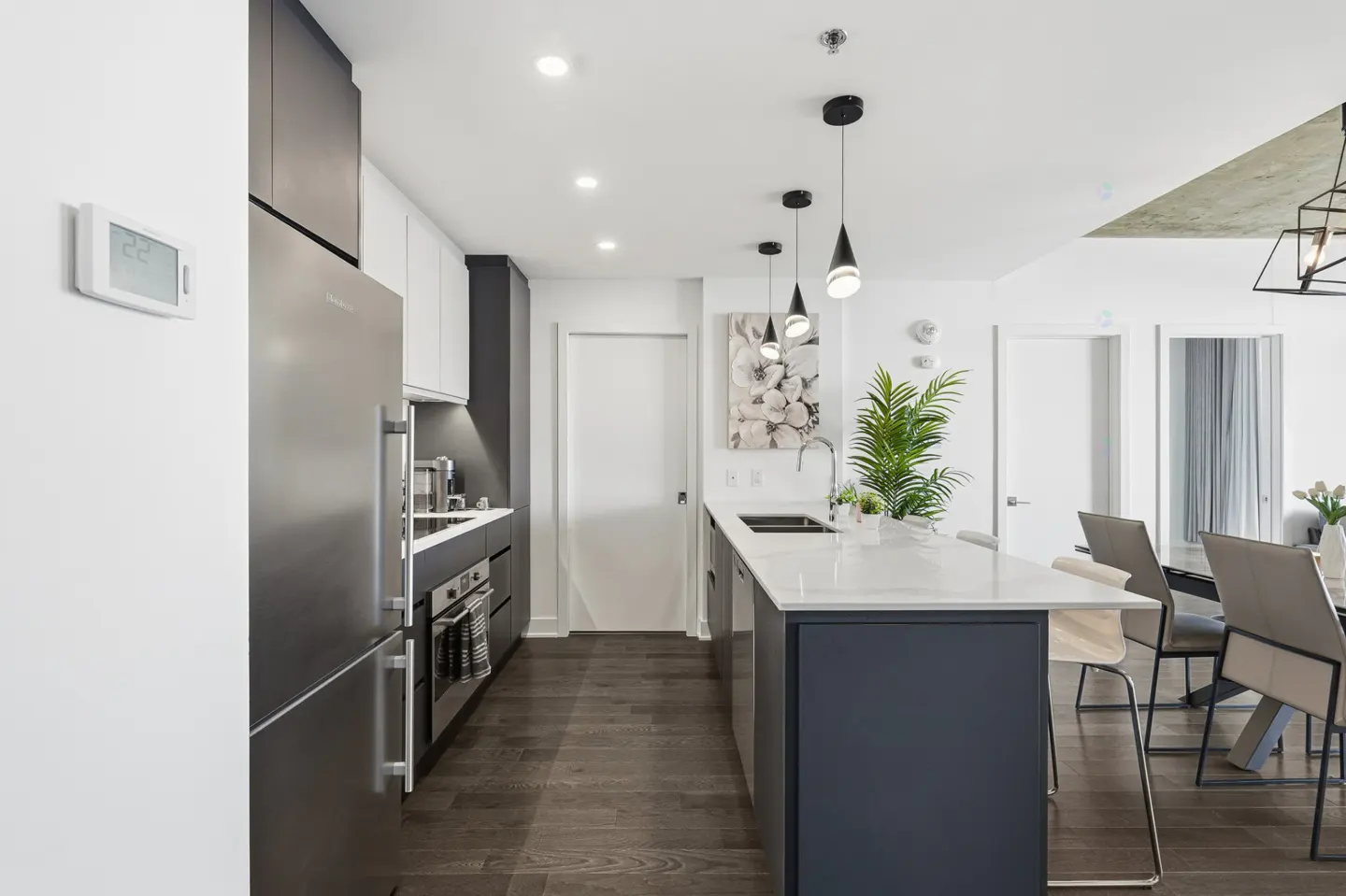 Modern kitchen with dark cabinets, stainless steel appliances, white quartz island, and dark wood floors.