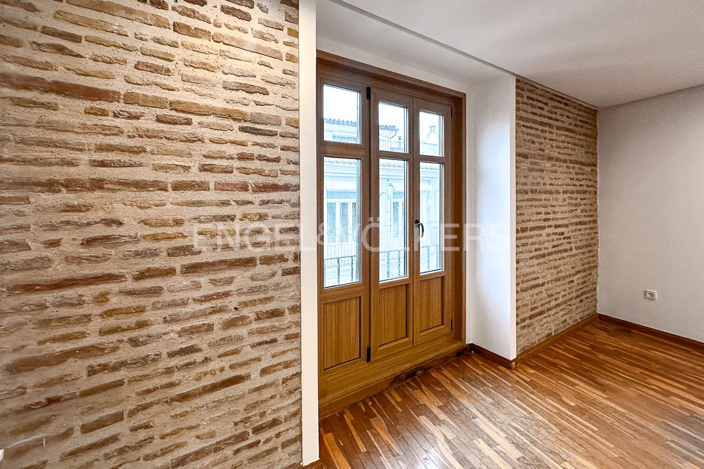 An empty room with brick walls, a wood floor, and a wood-framed window.