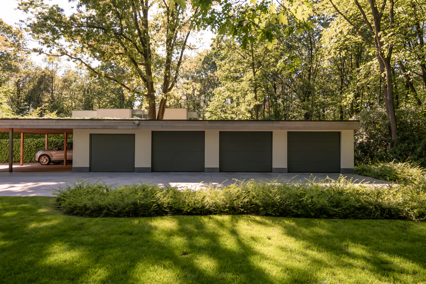 Four-car garage with gray doors and a carport with a car, surrounded by green lawn and trees.
