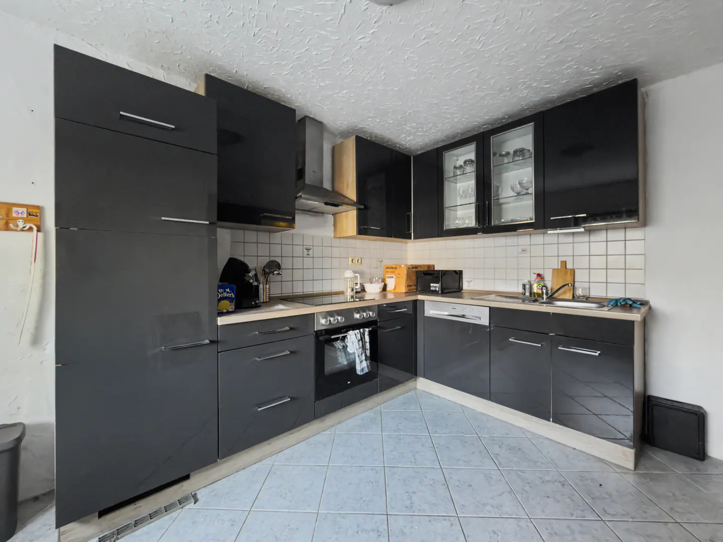 A modern kitchen with sleek, dark gray cabinets, stainless steel appliances, and light blue tile flooring.