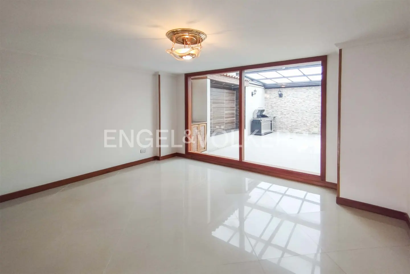 Empty room with white walls, glossy tile floor, and wood trim. Sliding glass doors lead to a patio with a grill.