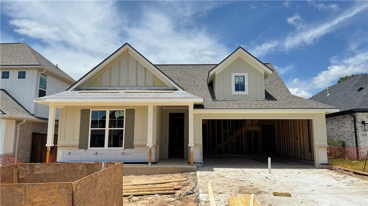 A new construction home with light beige siding, a gray roof, and an open garage under a bright blue sky.