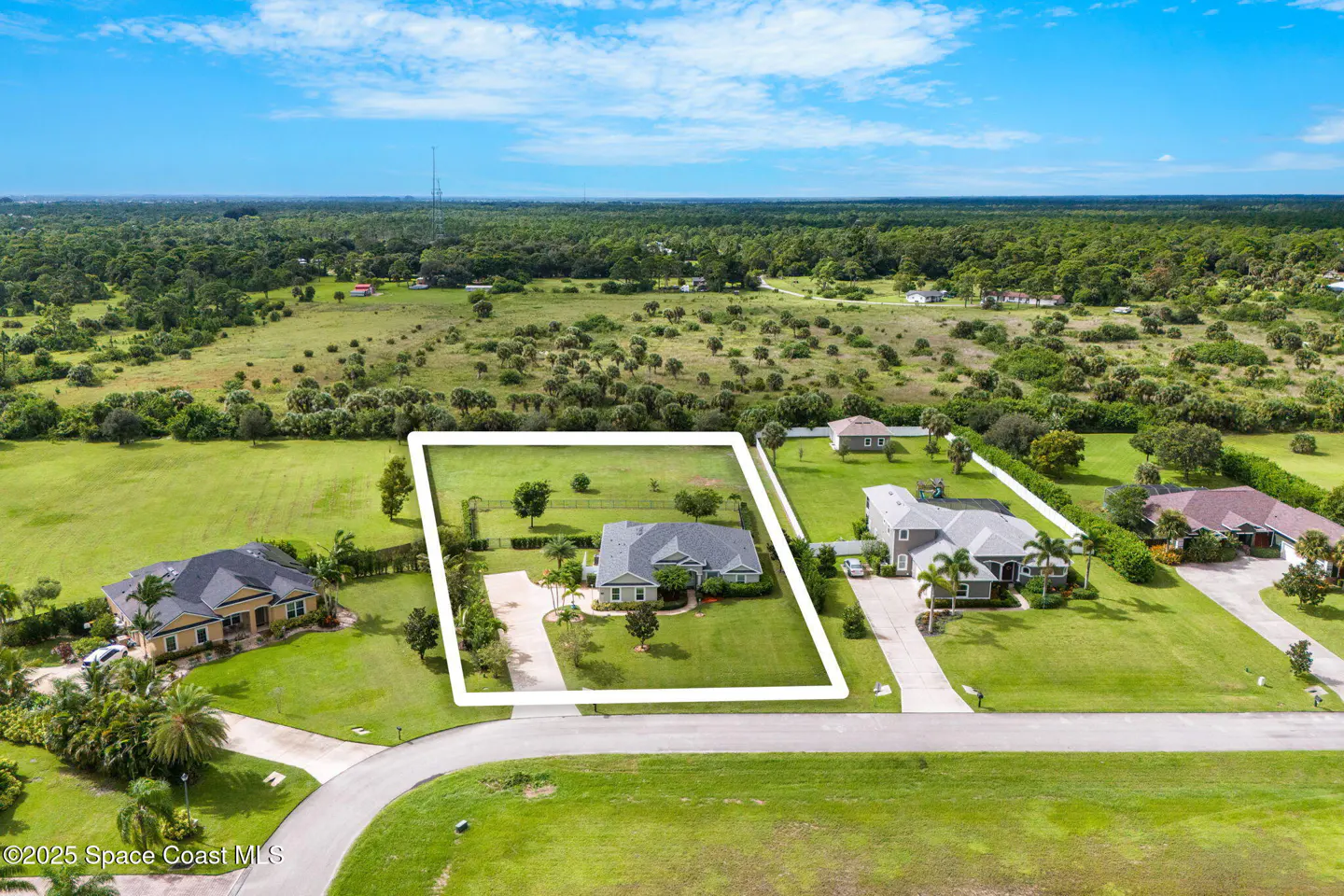 Aerial view of a gray house with a white border, green lawn, and trees under a blue sky.