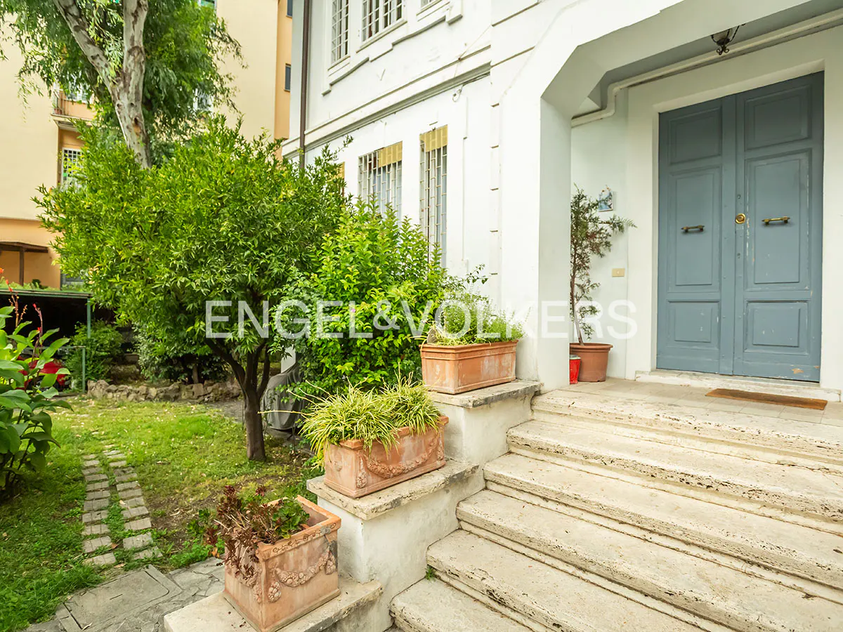 Exterior view of a white house with a blue door, stone steps, and potted plants.