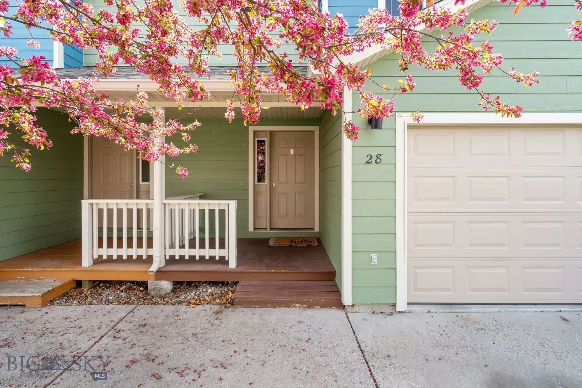A light green house with a beige door and garage, number 28, and pink blossoms.