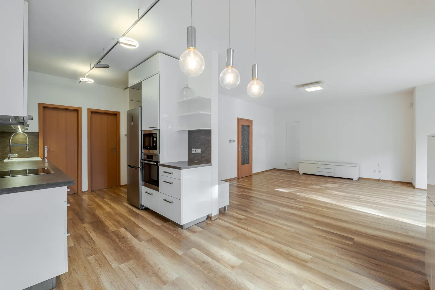 Bright, modern apartment with wood floors. White kitchen cabinets, stainless steel appliances, and globe pendant lights. Open floor plan.