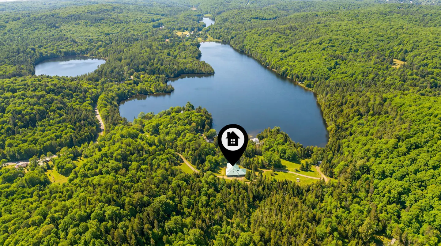 Aerial view of a house surrounded by green trees and a lake, marked with a location pin.