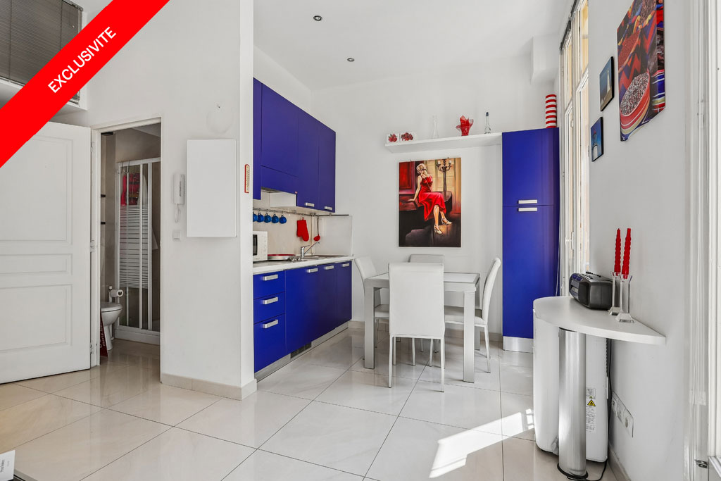 Modern kitchen with vibrant blue cabinets, white dining set, and a painting of a woman in a red dress on the wall.