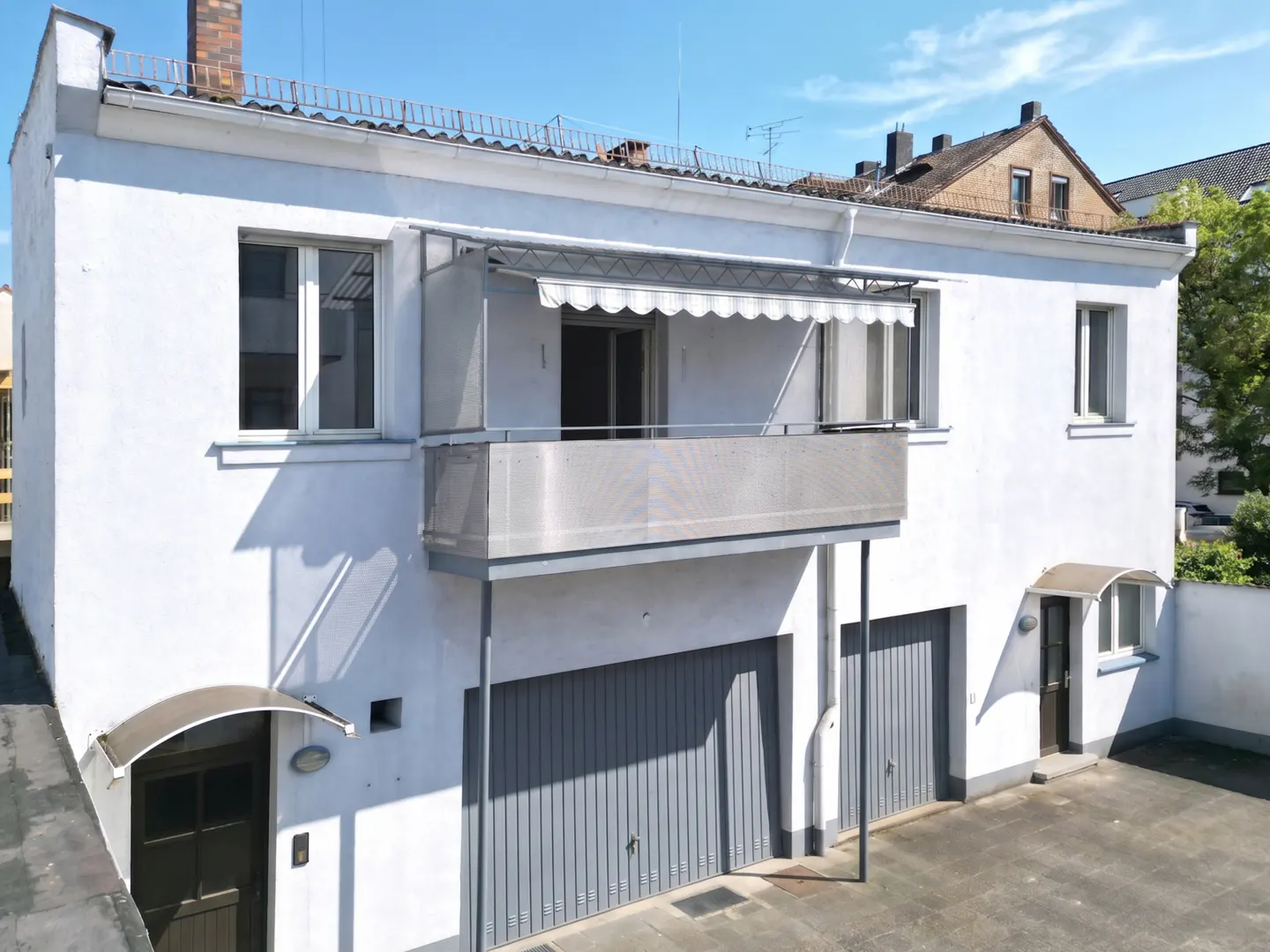 Exterior view of a two-story white building with a balcony, gray garage doors, and a small entrance door.