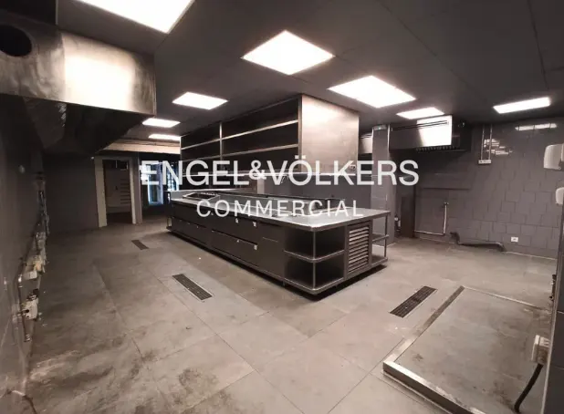 A commercial kitchen with stainless steel island, gray tile floor, and bright overhead lighting.