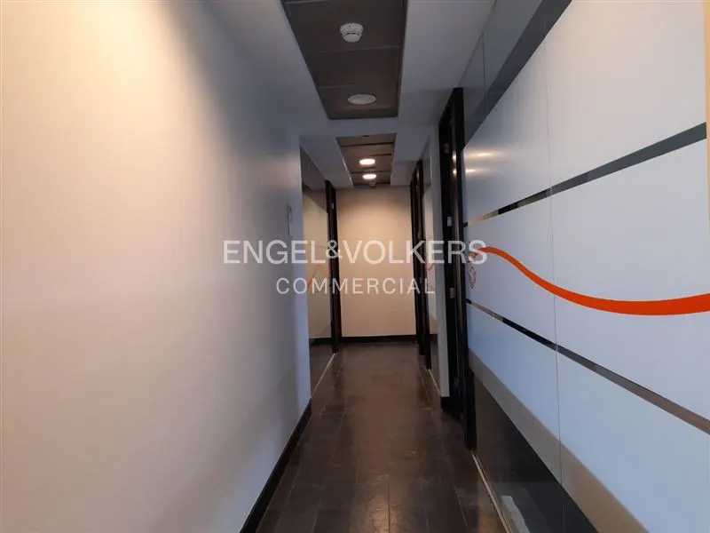Hallway view with white walls, dark flooring, and office doors with frosted glass and orange stripes.