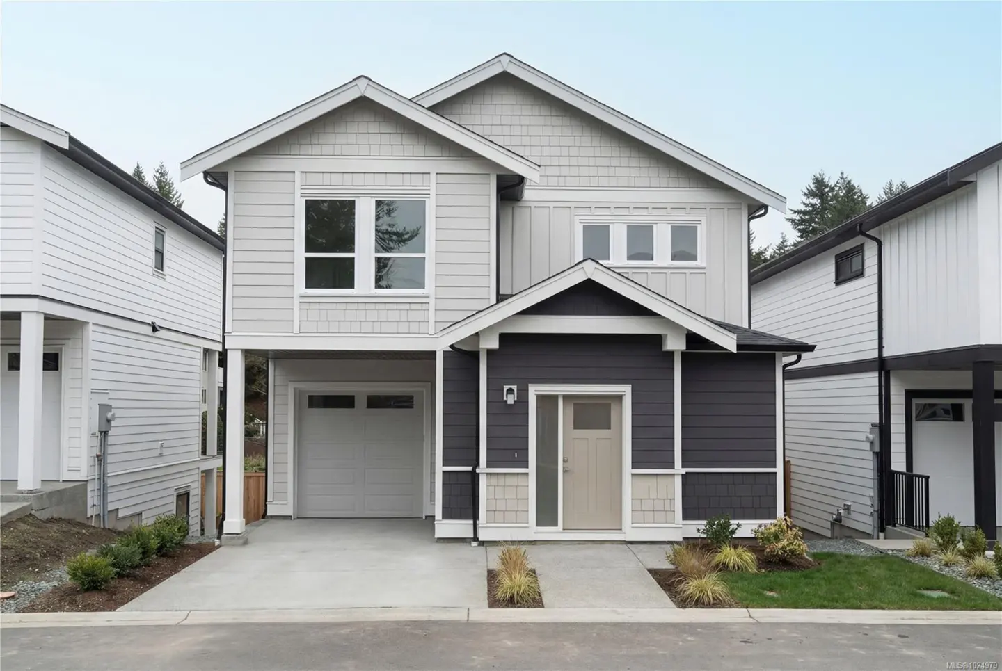 Two-story house with gray and dark gray siding, white trim, garage, and front door. Landscaping in front.
