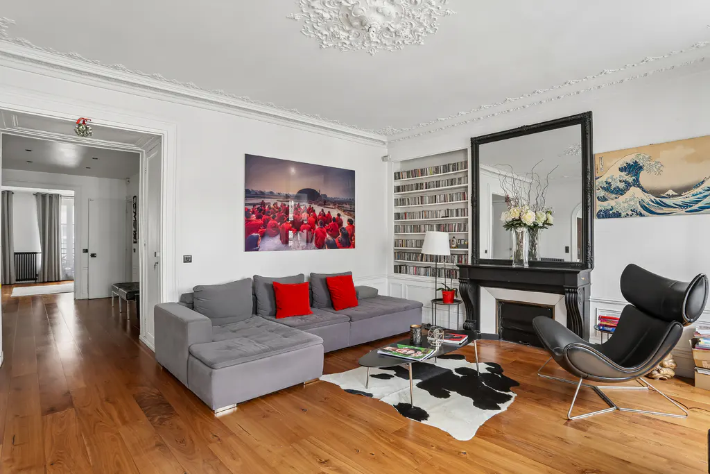 Bright living room with hardwood floors, gray sectional sofa with red pillows, black fireplace, and modern black chair.