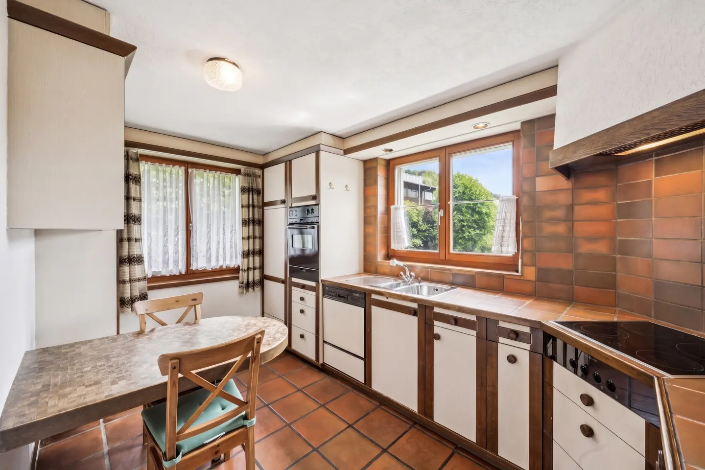 Kitchen with white and dark wood cabinets, terracotta tile floor, built-in oven, sink, and a small wooden dining table.