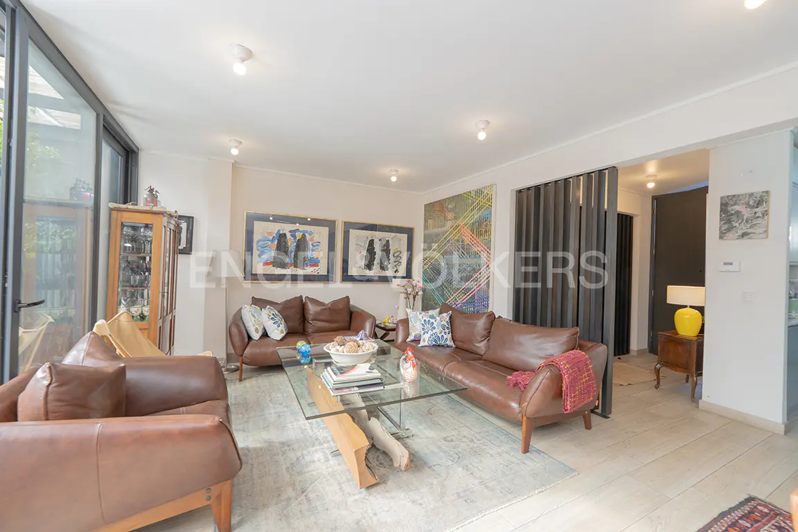 Living room with brown leather sofas, glass coffee table, and art. Natural light from large windows. Neutral rug and wood floors.