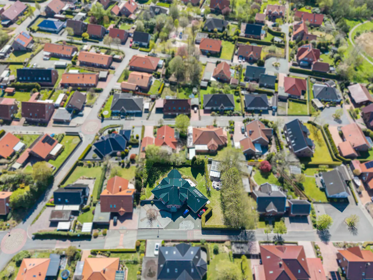 Aerial view of a suburban neighborhood with houses of varying colors and sizes, surrounded by green lawns and trees.