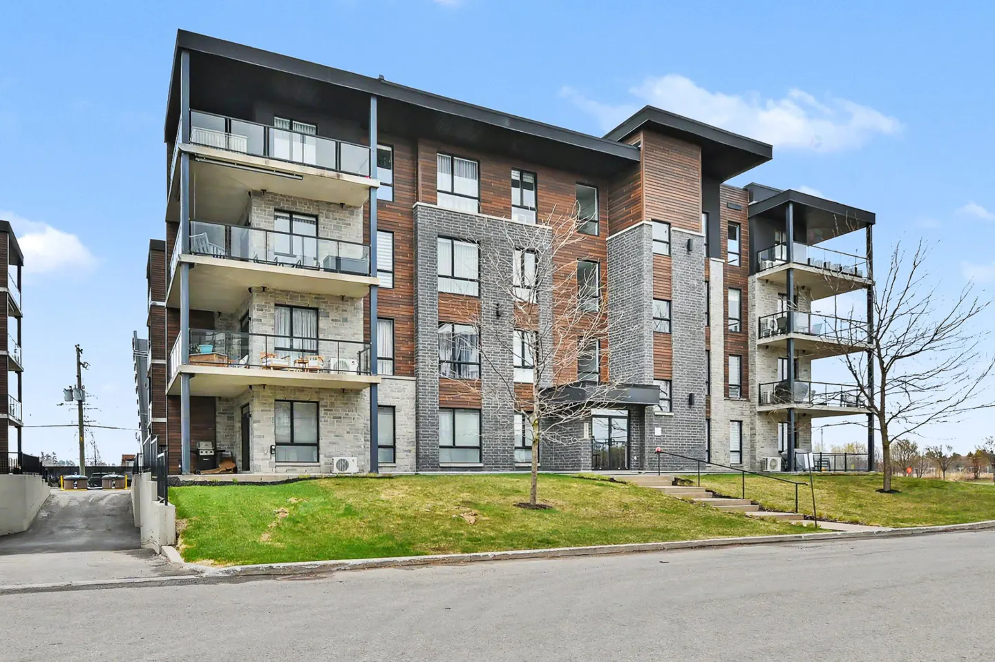 Modern apartment building with balconies, featuring gray brick and brown wood paneling under a blue sky.